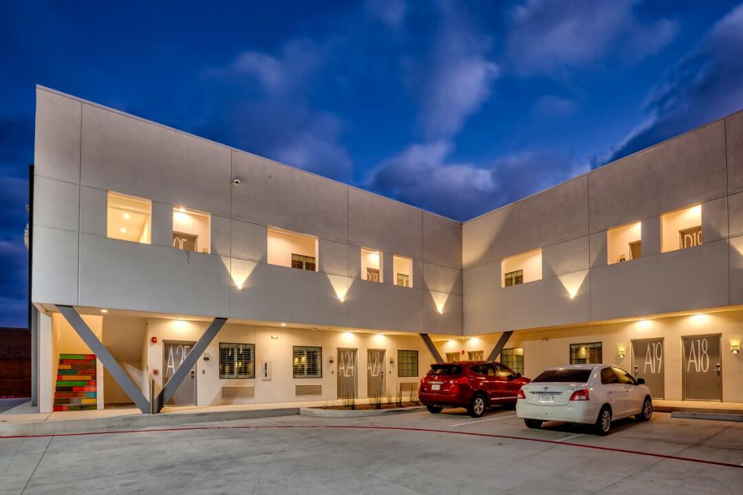 A modern hotel exterior at dusk with cars parked in front.