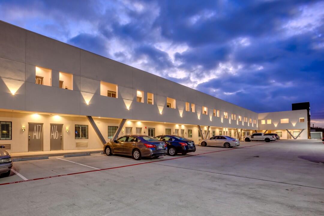 A two-story hotel building with a parking lot and cars parked outside at dusk.