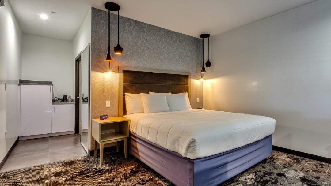 A hotel room with a bed, nightstand, refrigerator, and pendant lighting.