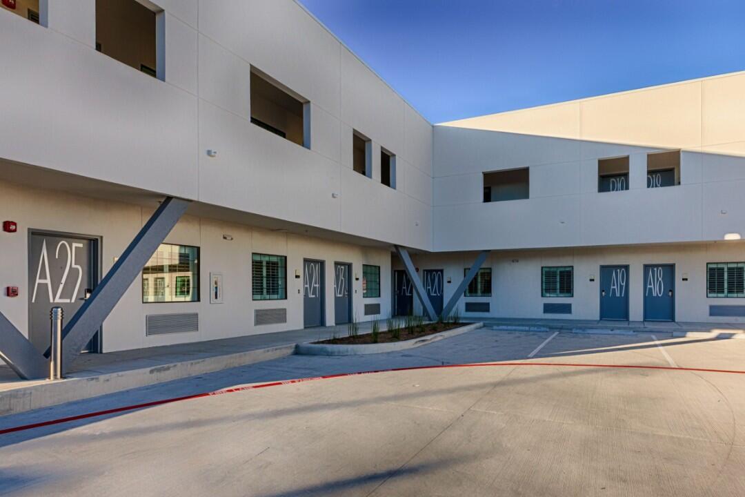 A white building with blue doors and windows, and a parking lot in front of it.