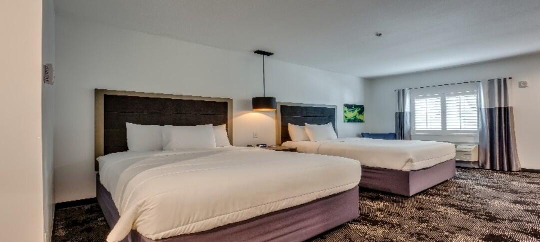 A hotel room with two beds, a pendant light, and a window.