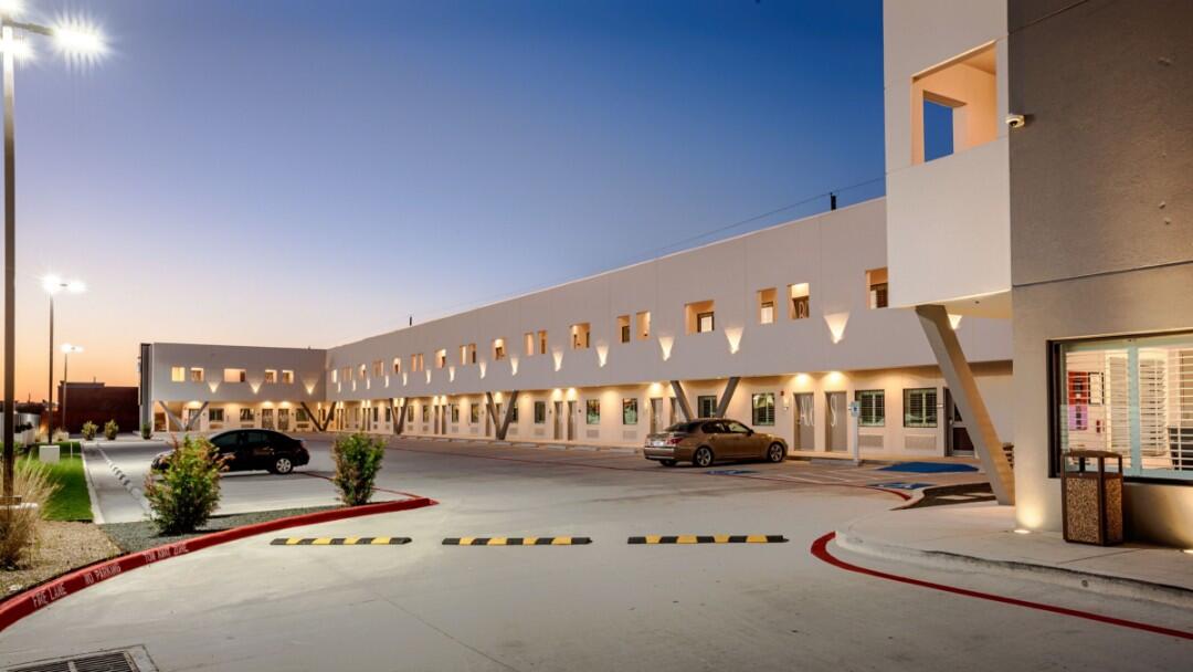 A wide exterior view of a hotel building with a parking lot at dusk.