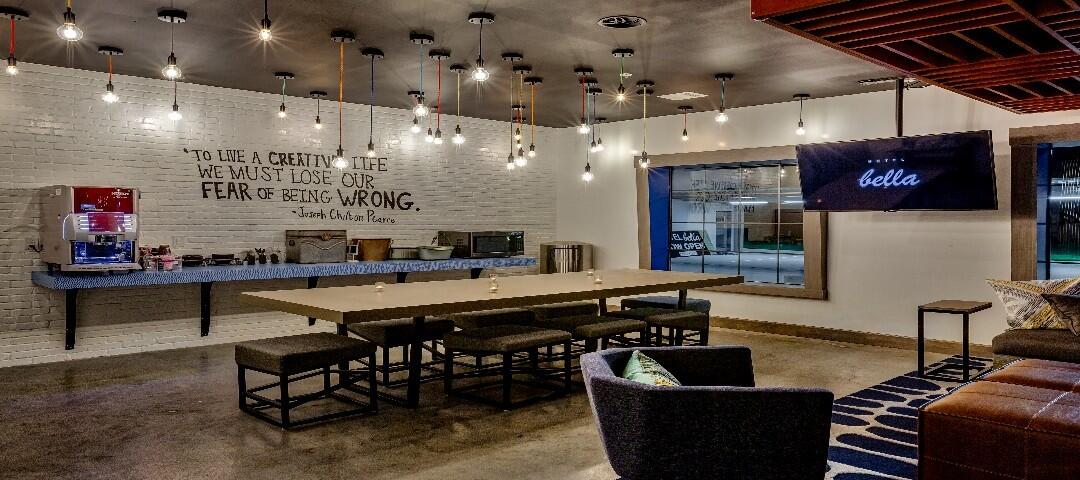A modern lounge area with a large table, comfortable seating, and a TV on the wall.