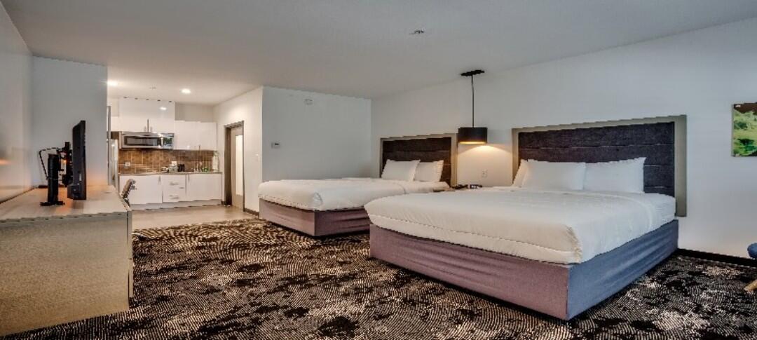 A wide view of a hotel room with two double beds, a kitchenette, and a TV on a counter.